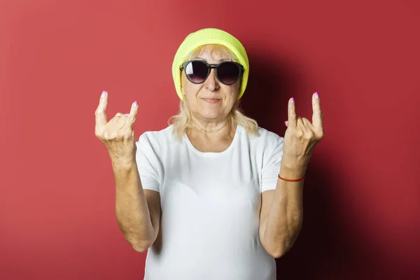 Rolig gammal kvinna i en hatt, gör en hand gest på en rosa bakgrund. Concept cool snygg mormor, modern stil — Stockfoto