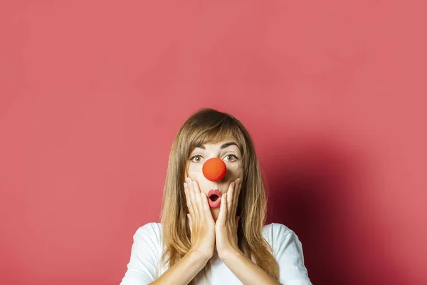 Young beautiful woman with a red nose of a clown on a pink background. Concept red nose day, holiday, party, clown — Stock Photo, Image