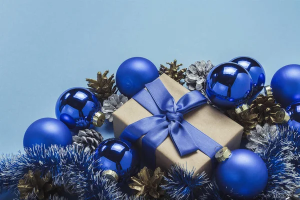 Подарочная коробка с голубой лентой, рождественские елки украшения, шары и белые и золотые шишки сосны на синем фоне. Концепция счастливого Рождества и Нового года. Минимализм — стоковое фото