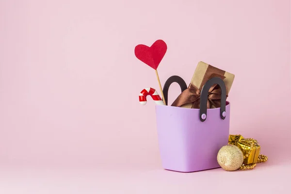 Pequeña bolsa de plástico para ir de compras, cajas de regalo, corazón en un palo, decoraciones de Navidad, fondo rosa. Concepto de compras pre-vacaciones, regalos para amigos y familiares, venta de Navidad — Foto de Stock