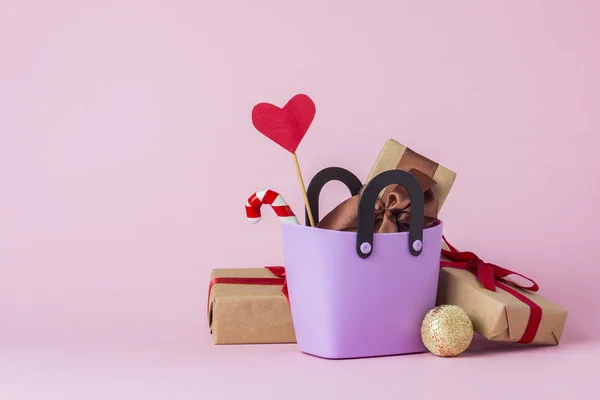 Small plastic bag for shopping, gift boxes, heart on a stick, Christmas decorations, pink background. Concept of pre-holiday shopping, gifts for friends and relatives, Christmas sale
