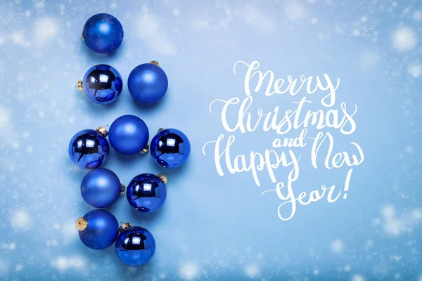 Blue Christmas tree toys, balls on a blue background with falling snow. Added text Merry Christmas and Happy New Year. Flat lay, top view