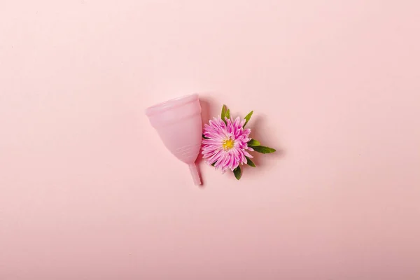 粉红色背景上的月经杯和花。月经的概念。平铺，顶部 — 图库照片