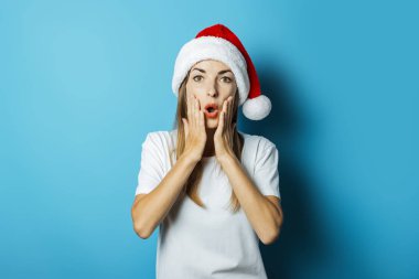Mavi bir arka plan üzerinde bir Noel Baba şapka sürpriz bir yüz ile Güzel Genç kadın. Yeni yıl ve noel için kavram fikri