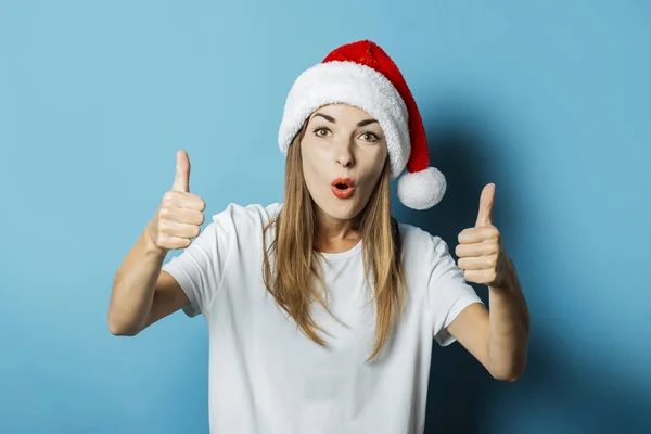 Hermosa mujer joven en el sombrero de Santa Claus hace gestos de la mano sobre un fondo azul. Concepto de idea para Año Nuevo y Navidad, regalos de Navidad — Foto de Stock