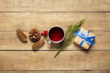 Sıcak çay, külahlı metal bardak, Noel ağacı filizi ve ahşap arka planda bir hediye. Kış havası, Noel, kış tatili kavramı. Düz yatış, üst görünüm