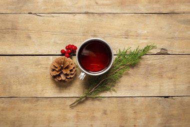 Sıcak çay, koni ve ahşap zemin üzerinde bir Noel ağacı filizi olan metal bir bardak. Sonbahar, kış, tatil, kamp, kış tatillerinin başlangıcı. Düz yatış, üst görünüm