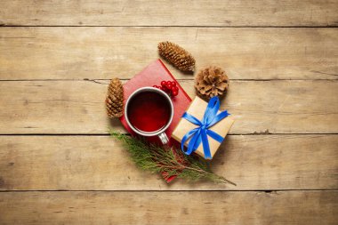 Sıcak çay, koni, Noel ağacı filizi, bir kitap ve ahşap arka planda bir hediye. Kış havası, Noel, kış tatili kavramı. Düz yatış, üst görünüm