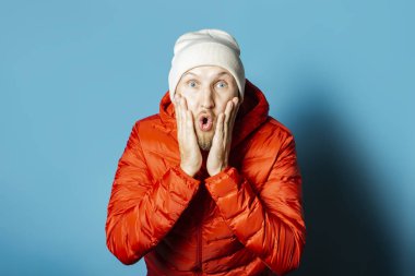 Şapkalı, kırmızı ceketli, mavi şapkalı, şaşırmış bir adam.