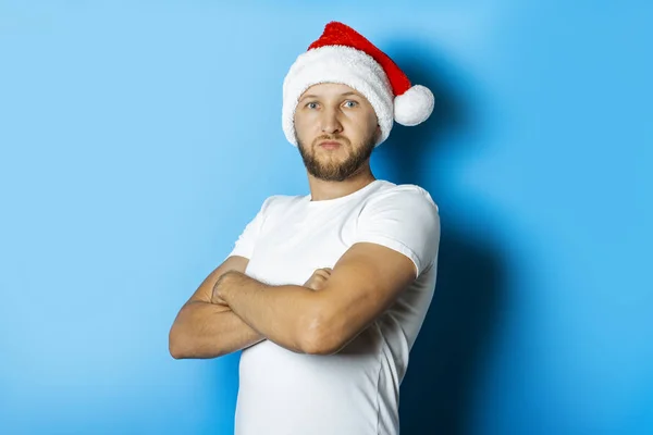 Mann mit Weihnachtsmann-Hut und verschränkten Armen auf blauem Hintergrund. — Stockfoto