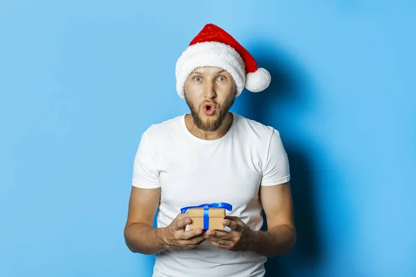 Mann mit überraschtem Gesicht im Weihnachtsmann-Hut hält Geschenke in der Hand — Stockfoto