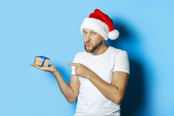 Man in a Santa Claus hat is holding a gift on a blue background. — Stock Photo, Image