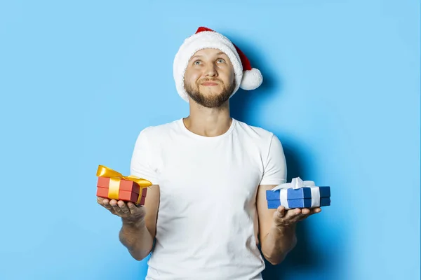 Mann mit nachdenklichem Gesicht im Weihnachtsmann-Hut hält Geschenke in der Hand — Stockfoto