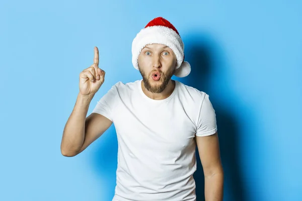 Mann mit überraschtem Gesicht in Weihnachtsmann-Mütze auf blauem Rücken — Stockfoto