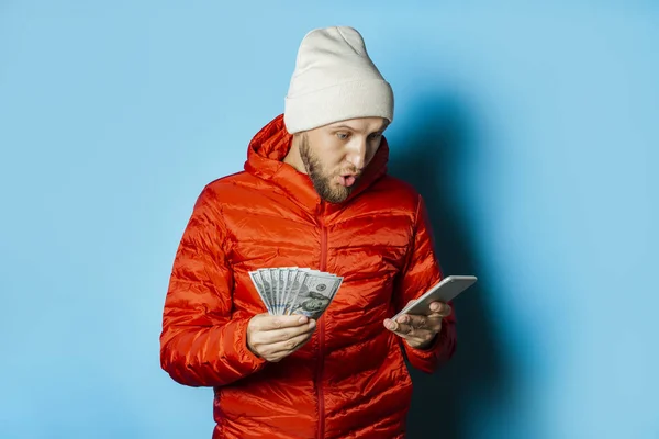 Man with a surprised face in a hat and a red jacket holds money