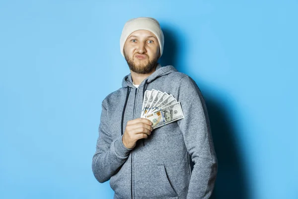 Man with a surprised face in a hoodie and hat is holding money o