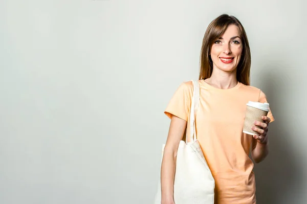 一个拿着购物袋的年轻女人 手里拿着一个纸杯 上面有淡淡的咖啡 — 图库照片