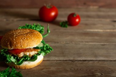 Tahta bir masada taze tavuk burger, domates ve marul..