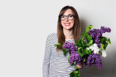 Gözlüklü genç mutlu kadın arka planda bir demet leylak tutuyor.