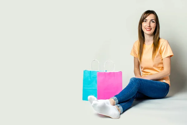 Young woman with a smile sits on the floor with bags for shopping on a light background. Banner.