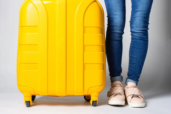 Frauenbeine Jeans Stehen Neben Einem Gelben Koffer Auf Hellem Hintergrund — Stockfoto