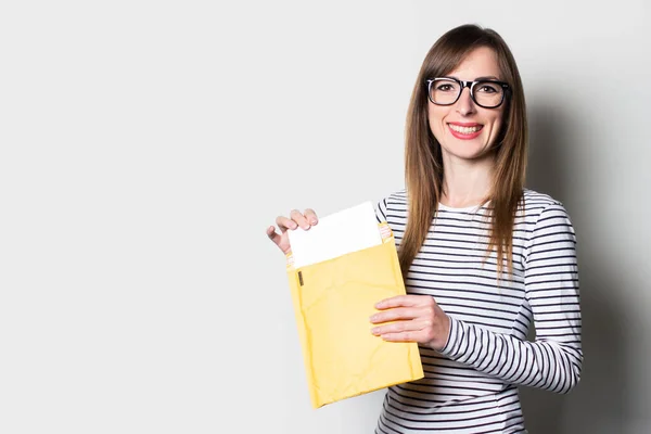 Young woman takes out a letter or notice from a paper envelope on a light background. Concept letter from college, taxes.