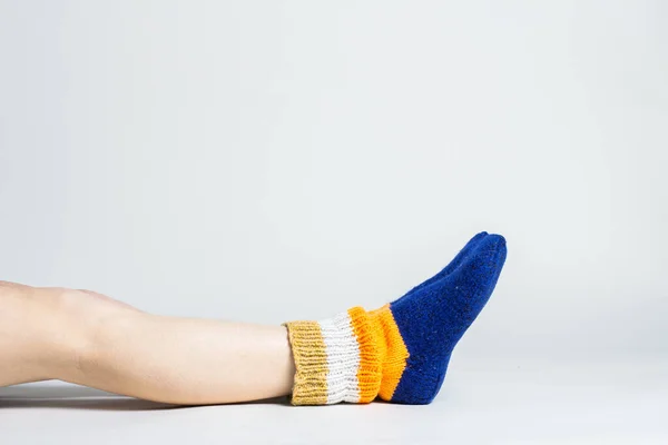 Woman sits on the floor in warm multi-colored socks on a light background. Only legs visible.