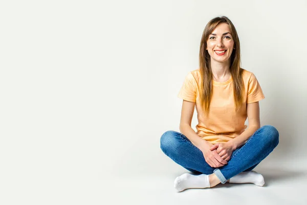 Young woman with a smile sits on the floor on a light background. Banner.