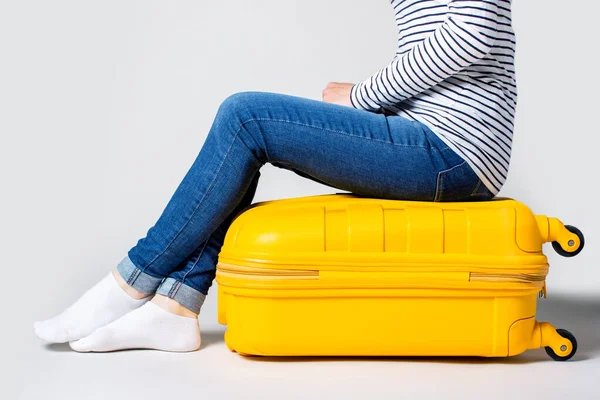 Frau Sitzt Auf Einem Gelben Plastikkoffer Vor Hellem Hintergrund Reisekonzept — Stockfoto