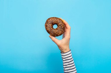 Kadın eli mavi arka planda donut tutuyor. Şekerleme dükkanı, hamur işleri, kahve dükkanı. Pankart. Düz yatış, üst görünüm.