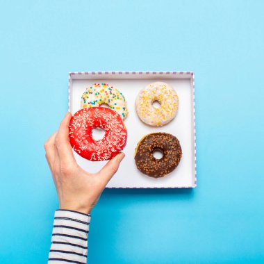 Kadın eli mavi arka planda donut tutuyor. Şekerleme dükkanı, hamur işleri, kahve dükkanı. Pankart. Düz yatış, üst görünüm.