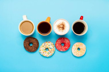 Lezzetli çörekler ve bardaklar sıcak içecekler, kahve, kapuçino, mavi arka planda çay. Şeker, fırın, hamur işi, kahve dükkanı, toplantı, arkadaşlar, arkadaş takımı kavramı. Düz yatış, üst görünüm.