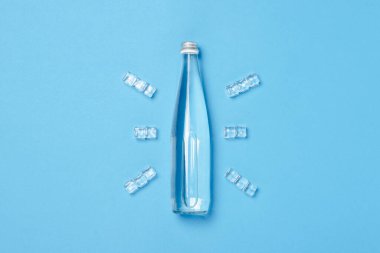 Buz küpleriyle mavi arka planda berrak su bulunan cam şişe. Sağlık ve güzellik kavramı, su dengesi, susuzluk, sıcaklık, yaz. Düz yerde, üst tarafta. Pankart.