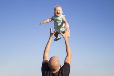 Babası çocuğunu mavi gökyüzüne fırlatıyor. Çocuklarla konsept oyun, mutlu aile.