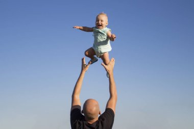 Babası çocuğunu mavi gökyüzüne fırlatıyor. Çocuklarla konsept oyun, mutlu aile.