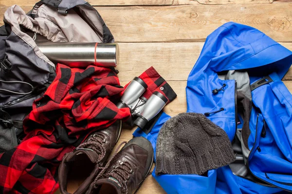 Hiking boots, jacket, binoculars, shirt, hat, backpack on a wooden background. The concept of hiking, tourism, camp, mountains, forest. Banner. Flat lay, top view.