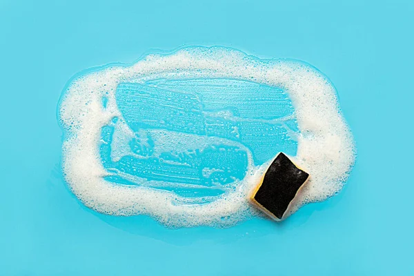 Soap foam from a cleaning agent and a cleaning sponge on a blue background. Cleaning concept, cleaning service. Flat lay, top view.