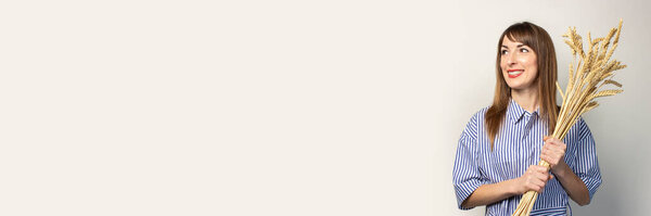 молодая девушка в синем платье держит букет сухих колосьев пшеницы на светлом фоне. Девушка проявляет эмоции. Баннер. Концепция косметологии, сбора урожая, фермы
.