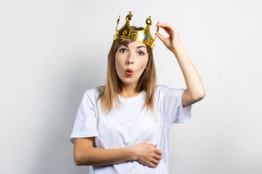 Kafasında taç olan genç bir kadın, hafif bir arka planda şaşırmış bir yüz. Duygusal kahkaha, sürpriz, şok. Kraliçe kavramı, şans, servet, kazanç, zafer, hayal, amaç, arzu. Pankart.