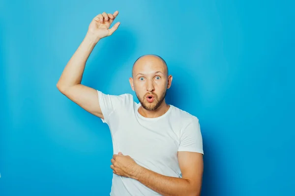 Young man in a white T-shirt with wet armpits from sweat on a blue background. Concept of excessive sweating, heat, deodorant.