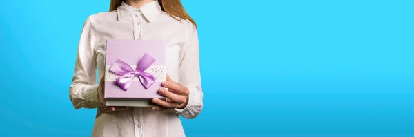 A young girl opens a gift box in front of her on a light blue background. The face of the girl is not visible.