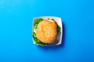 Parlak mavi arka planda taze bir burger. Düz yatış, üst görünüm.