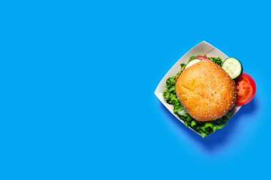 Taze hamburger, salatalık, parlak mavi arka planda domates. Düz yatış, üst görünüm.