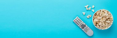 Mavi arka planda patlamış mısır ve uzaktan kumandalı televizyon kasesi. Ev sineması, sinema, boş zaman kavramı. Düz yatış, üst görünüm.