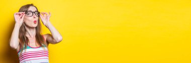 Genç kız sarı arka planda çizgili bir elbisede gözlük takarak dudak büküyor. Pankart.