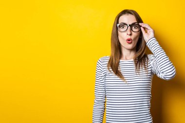 Sarı arka planda gözlük tutan genç bir kadın şok geçirdi.