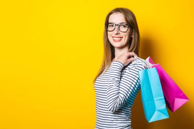 Sarı arka planda alışveriş torbalarıyla gülümseyen genç bir kadın. İnternetten alışveriş.