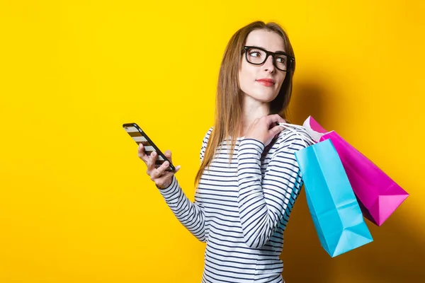 Mladá Žena Ohlédne Drží Telefon Nákupní Tašky Žlutém Pozadí — Stock fotografie