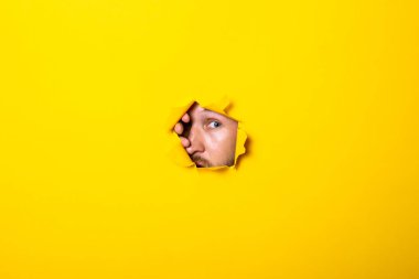 Genç adam sarı arka planda yırtık bir deliğe bakıyor..