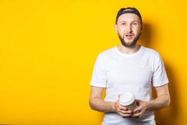 Sarı arka planda elinde kahve olan, kağıt bardaklı genç adam.